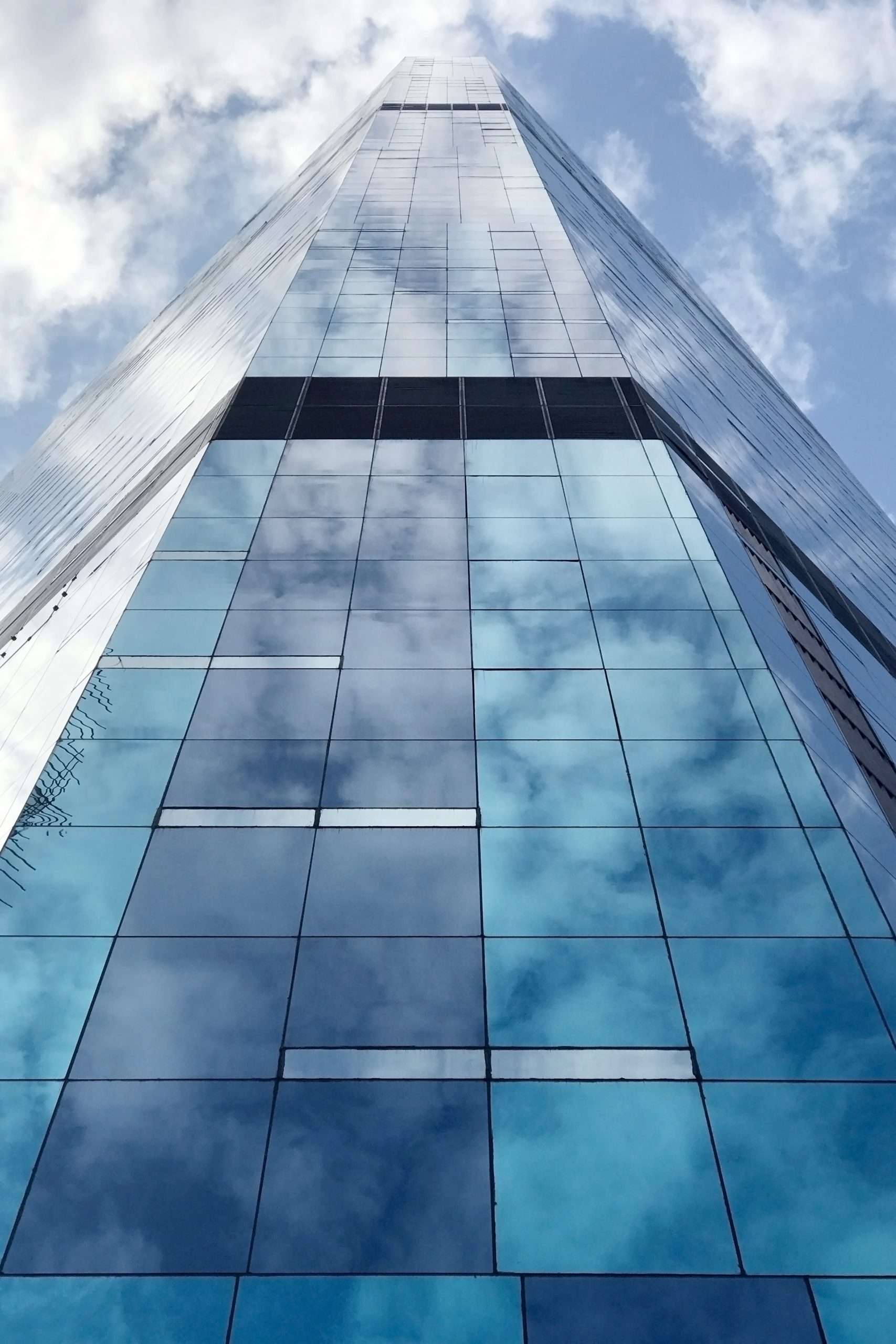 Moderne Glasfassade eines Hochhauses, die den Himmel spiegelt und für Transparenz, Leichtigkeit und technische Präzision steht. Das Bild symbolisiert die Expertise von vision4project in der Planung und Umsetzung innovativer Gebäudehüllen und Glasfassaden