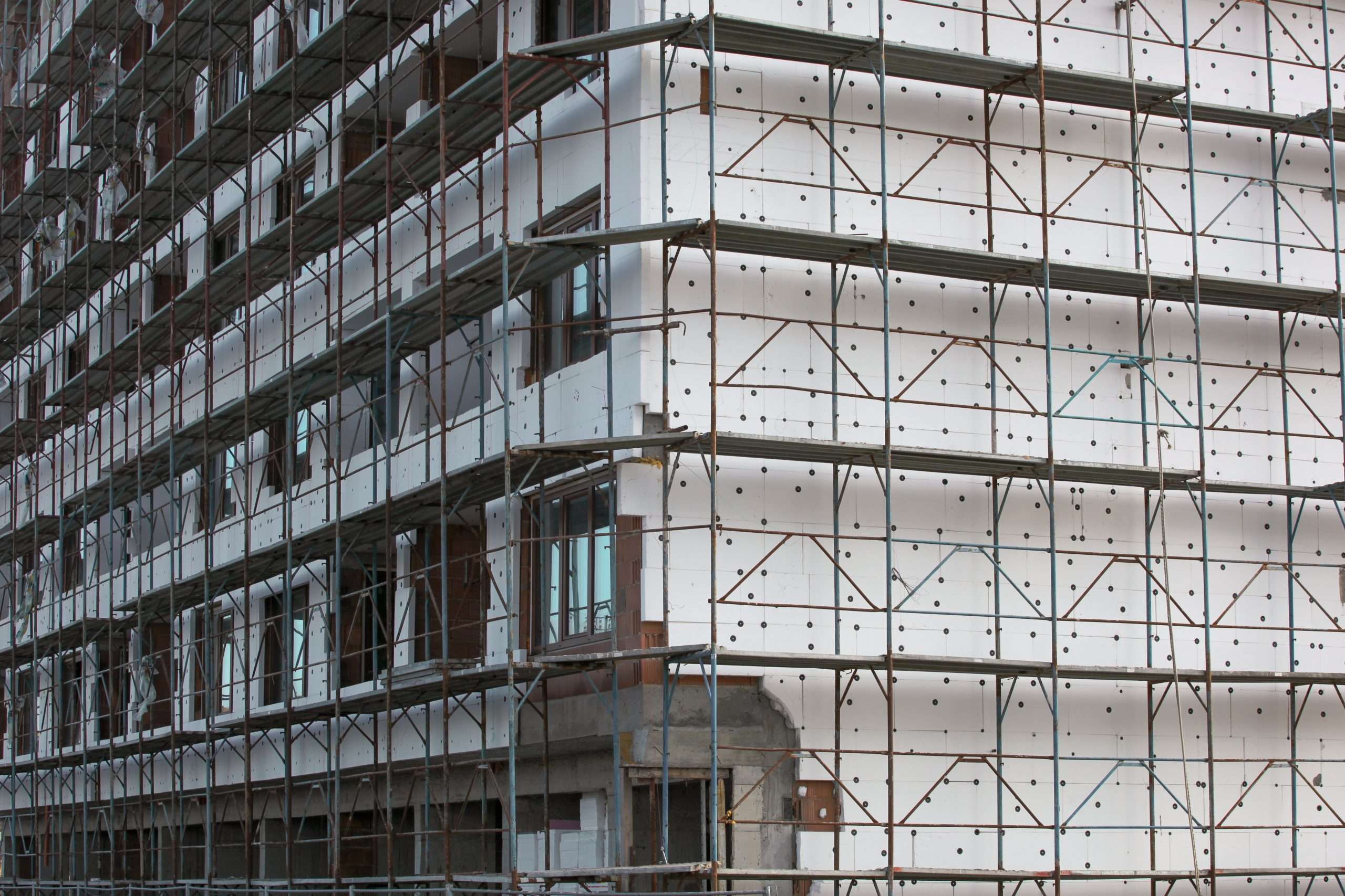 Fassade eines Gebäudes im Bauzustand mit Gerüst und sichtbarer Dämmung – Symbol für Fortschritt, Energieeffizienz und nachhaltige Bauweise. Das Bild steht für die Arbeit von vision4project an innovativen, technisch fundierten und zukunftsorientierten Lösungen im modernen Fassadenbau