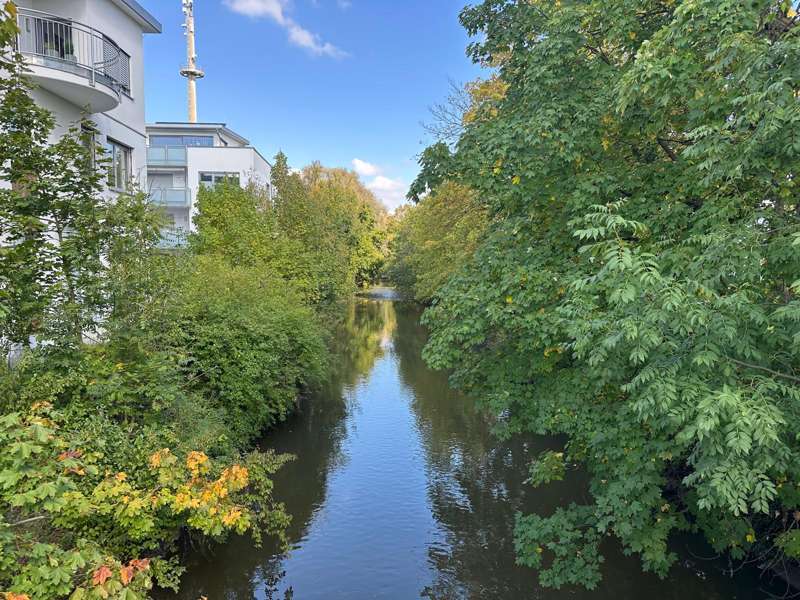 Ruhige Flusslandschaft mit modernen Gebäuden und herbstlicher Natur in Wertingen – Symbol für die digitale Innovationskraft und Nachhaltigkeit von Vision4Project.